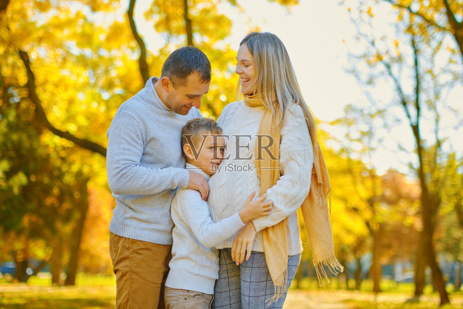 年轻的家庭，父母带着他们的儿子在秋天阳光明媚的公园里照片摄影图片