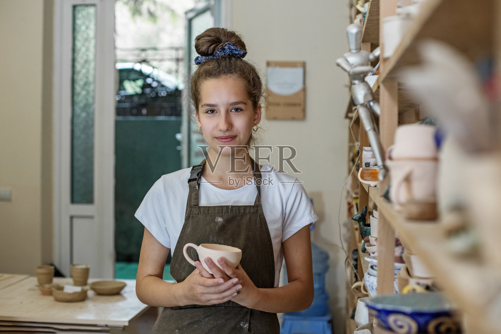 美丽的少女在陶器作坊玩模型泥。手工和泥塑艺术。照片摄影图片