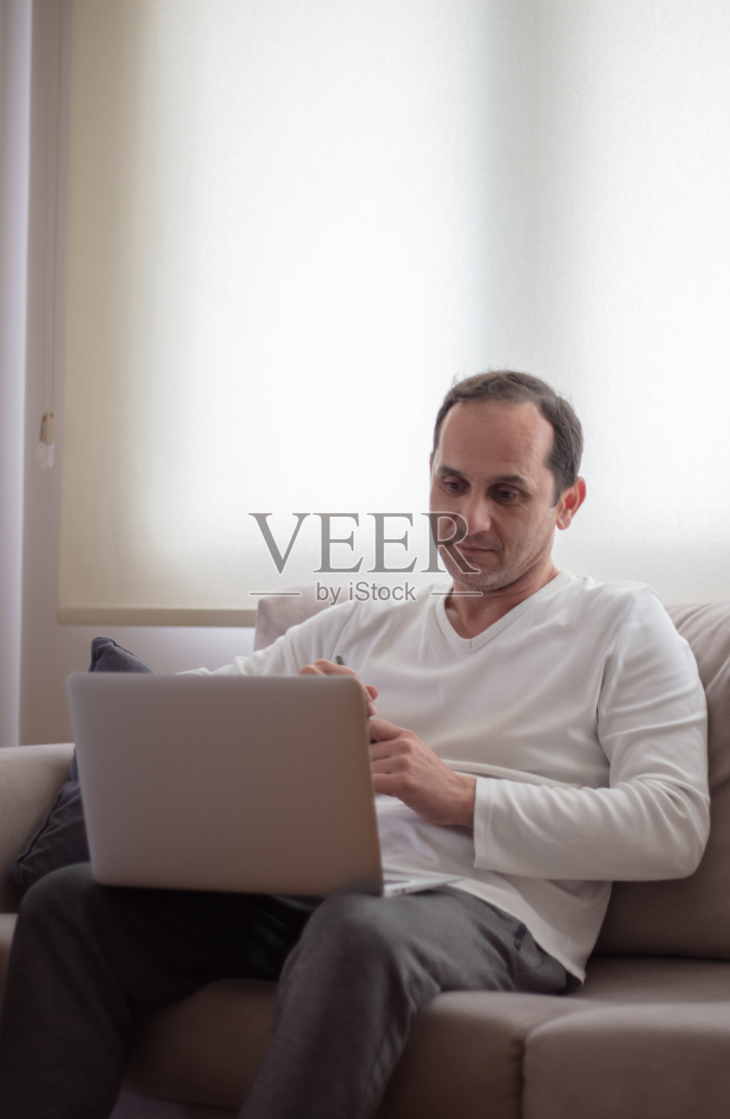 中年男子在家工作。他正坐在沙发上。照片摄影图片