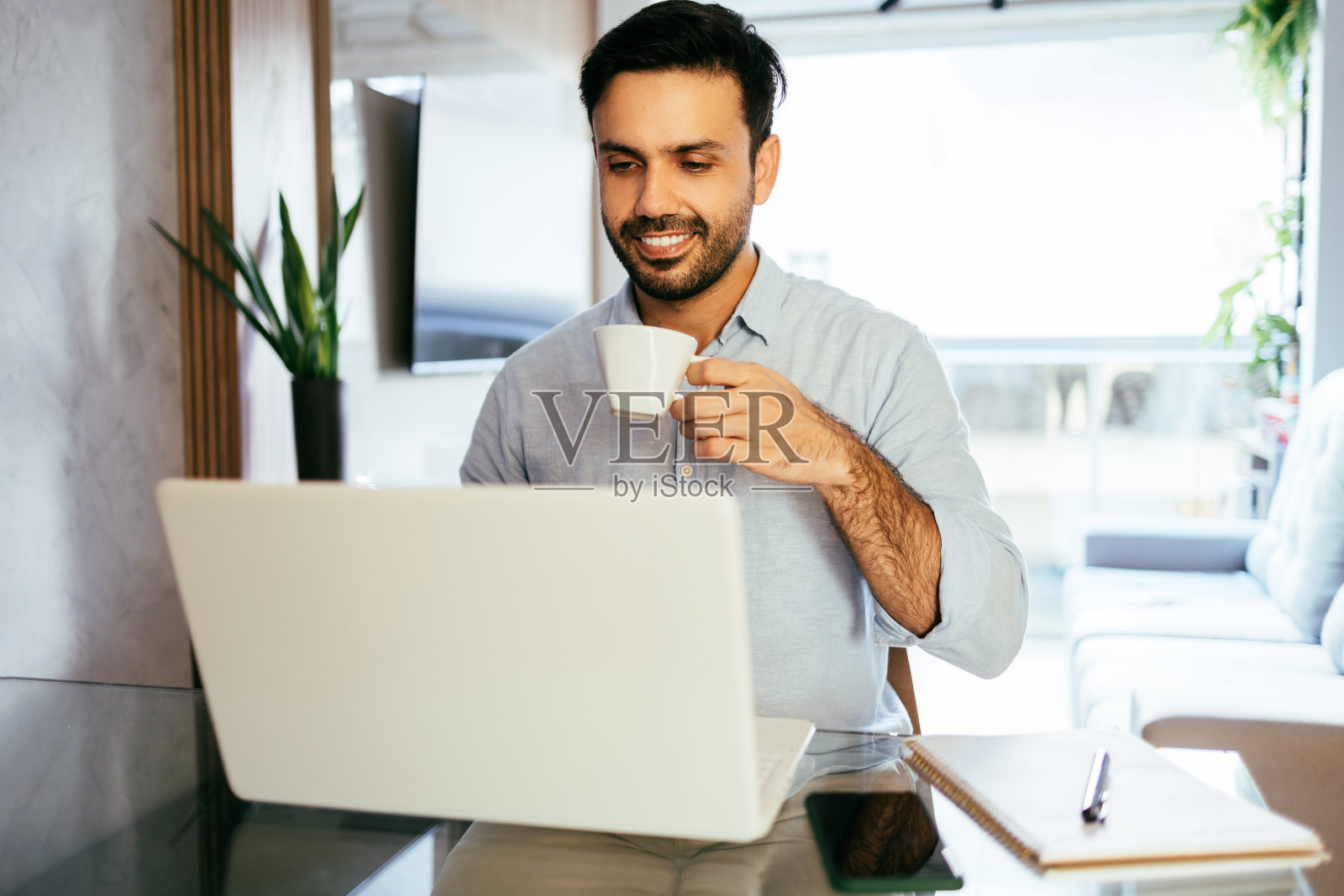 一名男子在家里用笔记本电脑工作，喝咖啡照片摄影图片