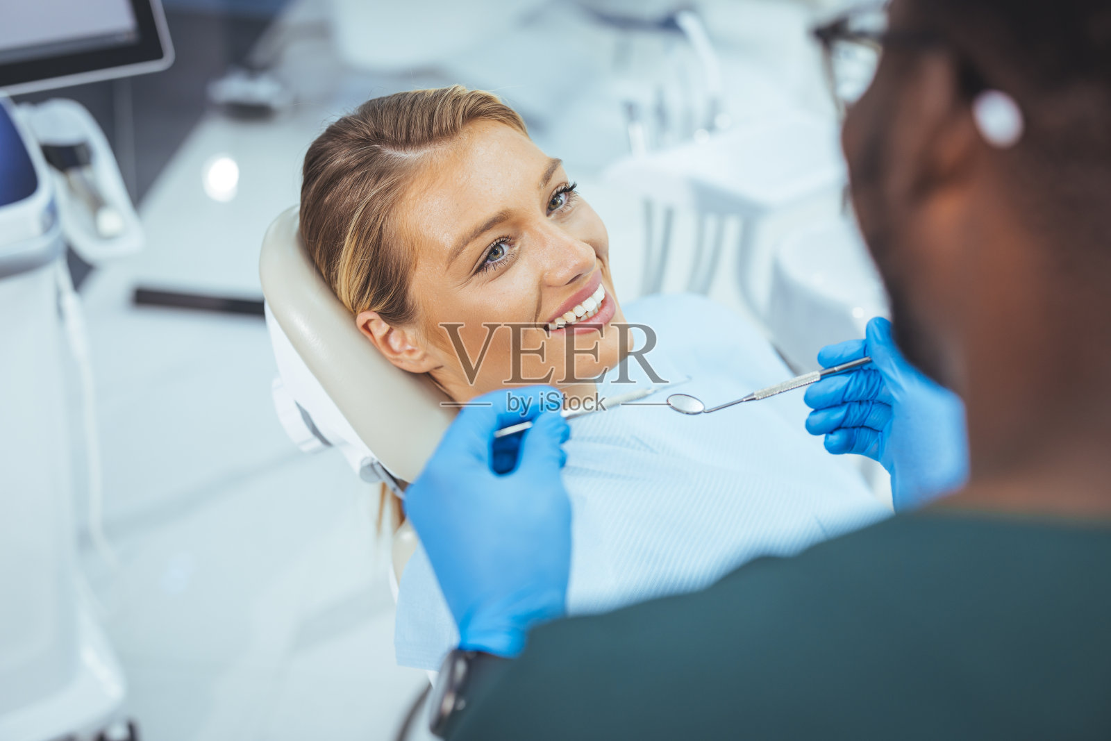 坐在牙医椅上的漂亮女士微笑着看着她的医生照片摄影图片