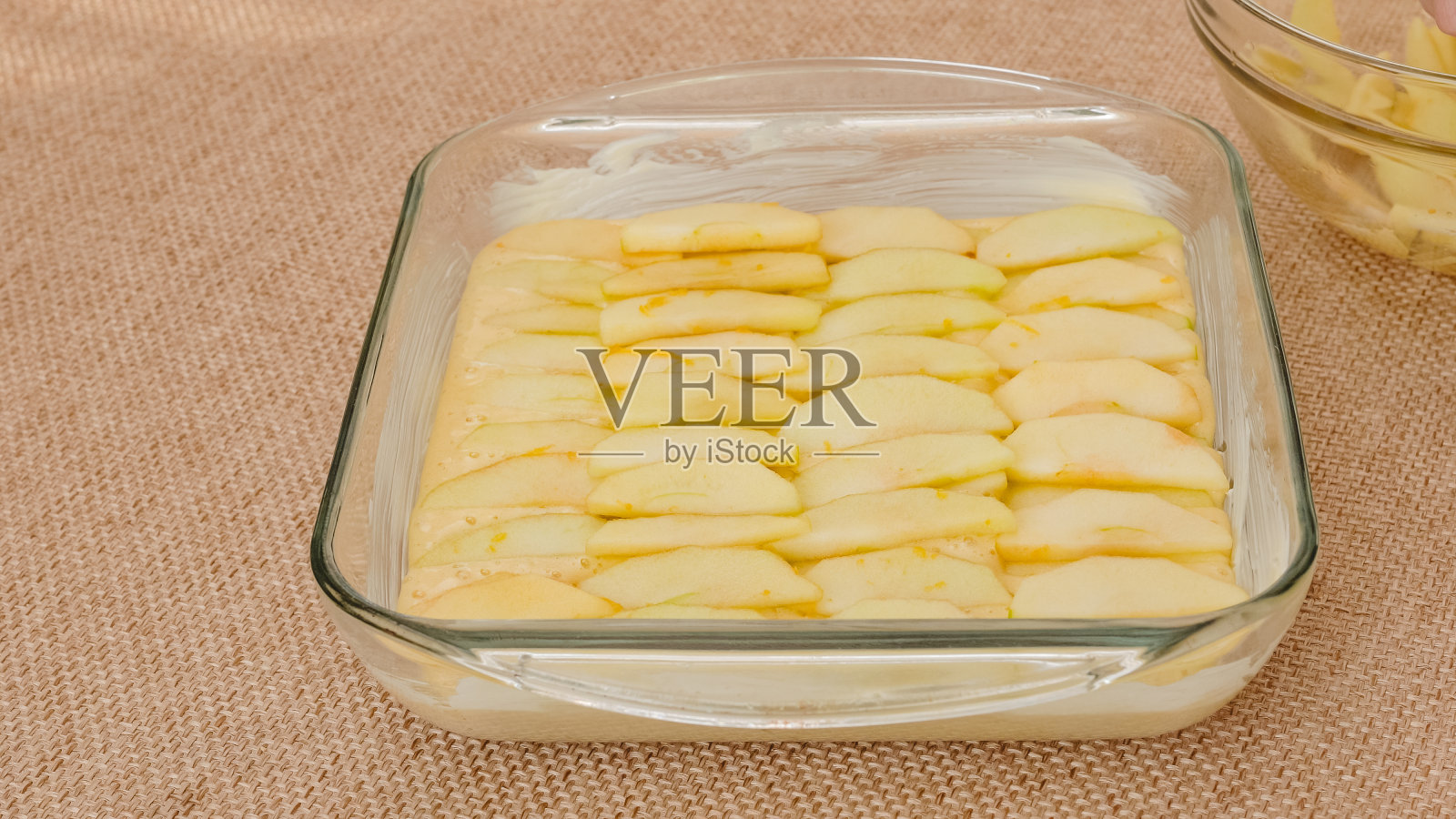 组装苹果蛋糕。把去皮的新鲜苹果片放在饼干面团上，紧挨着放在玻璃烤盘里照片摄影图片