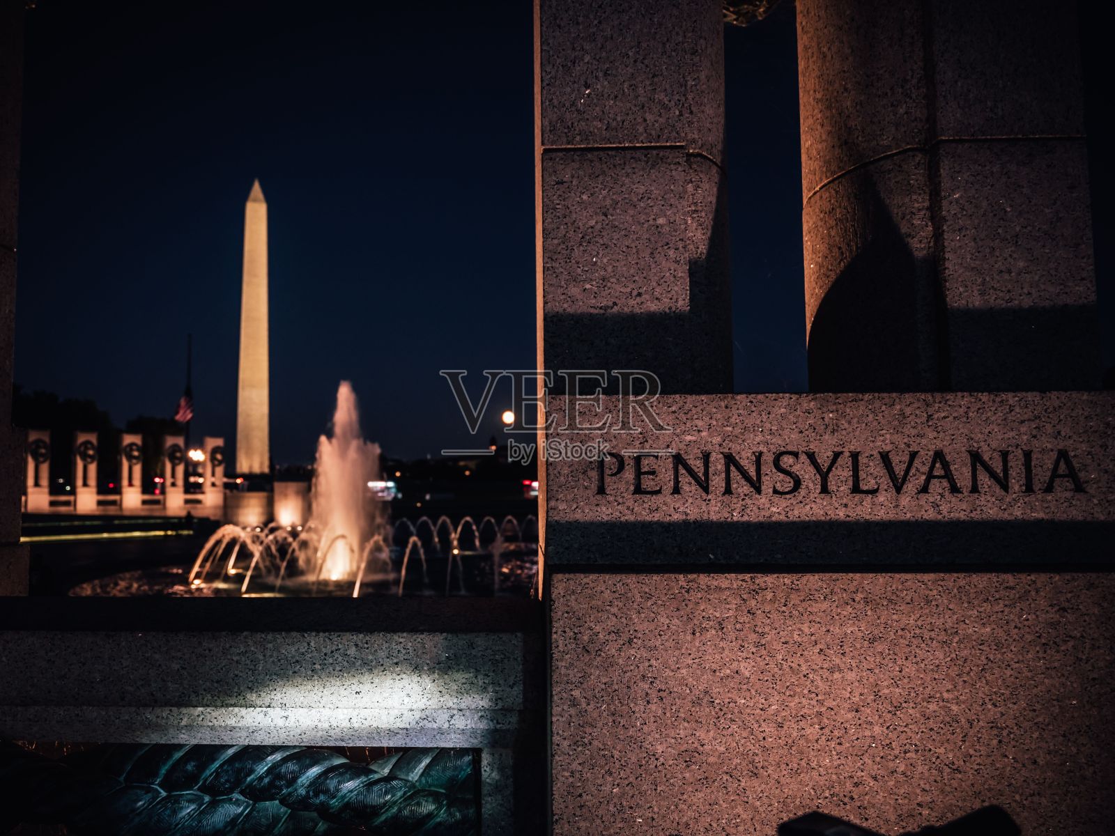 “宾夕法尼亚”刻在一块石头上，石头上有一个喷泉，晚上还刻有华盛顿纪念碑照片摄影图片