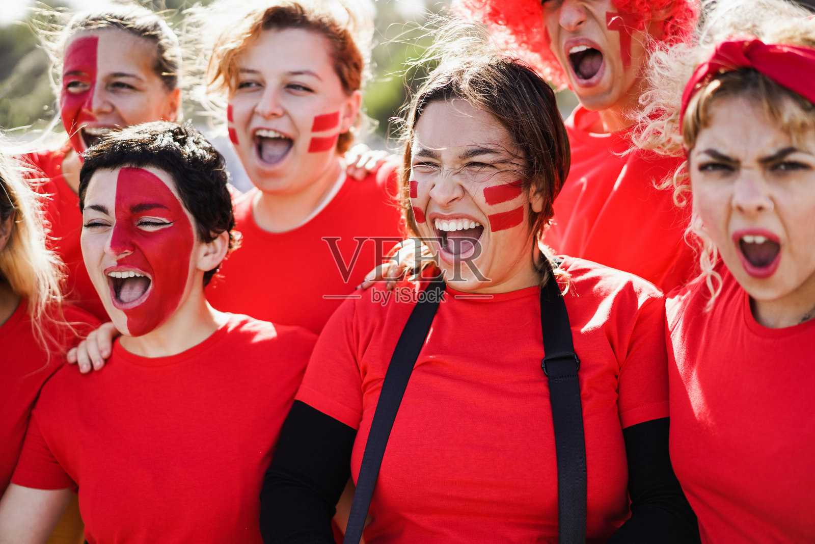 红色体育迷在支持自己的球队时尖叫-足球支持者在比赛活动中享受乐趣-注意中间女孩的脸照片摄影图片