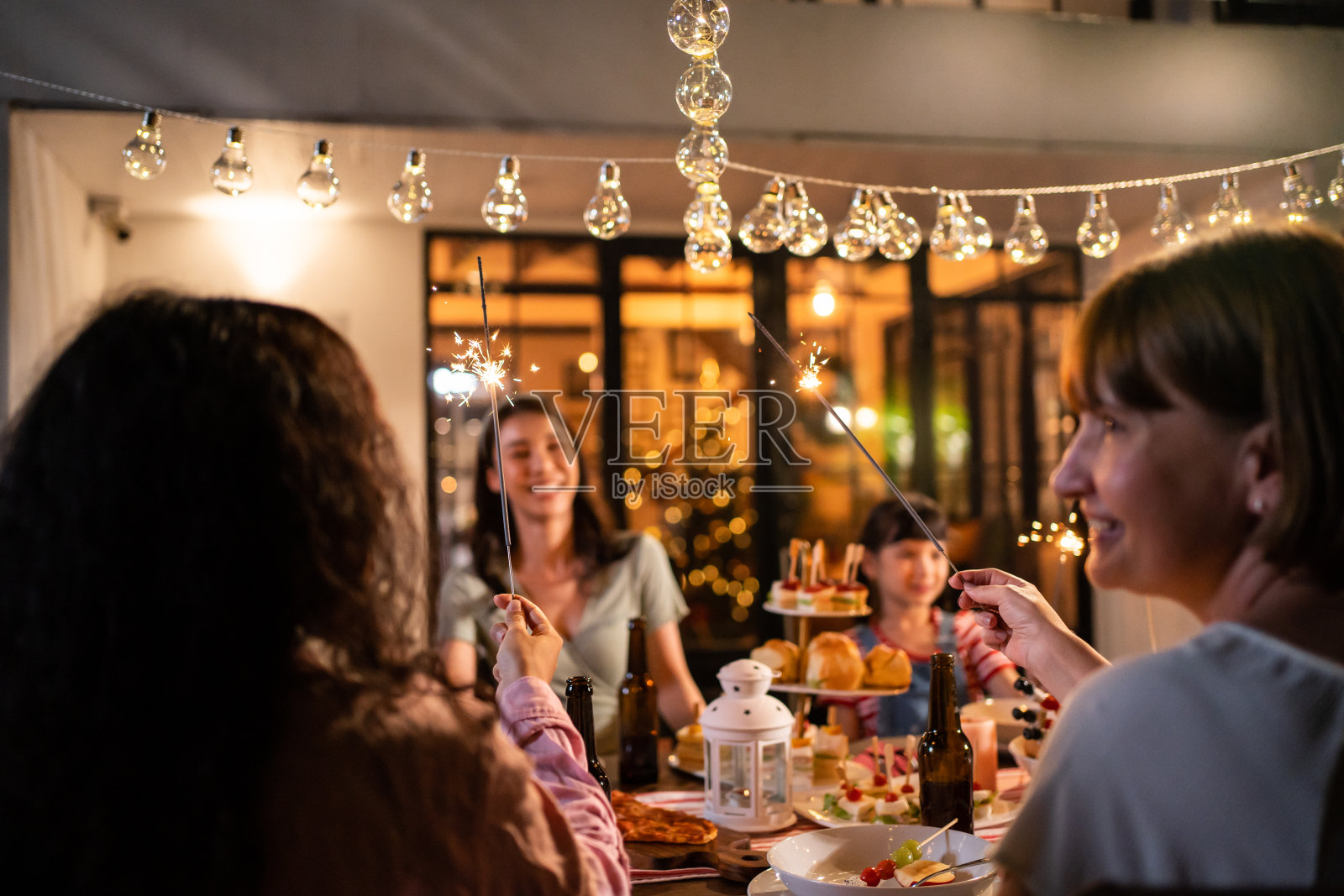 多民族大家庭在户外的花园中欢聚。迷人的各色人聚在餐桌前共进晚餐，吃着美食，庆祝周末团圆。照片摄影图片