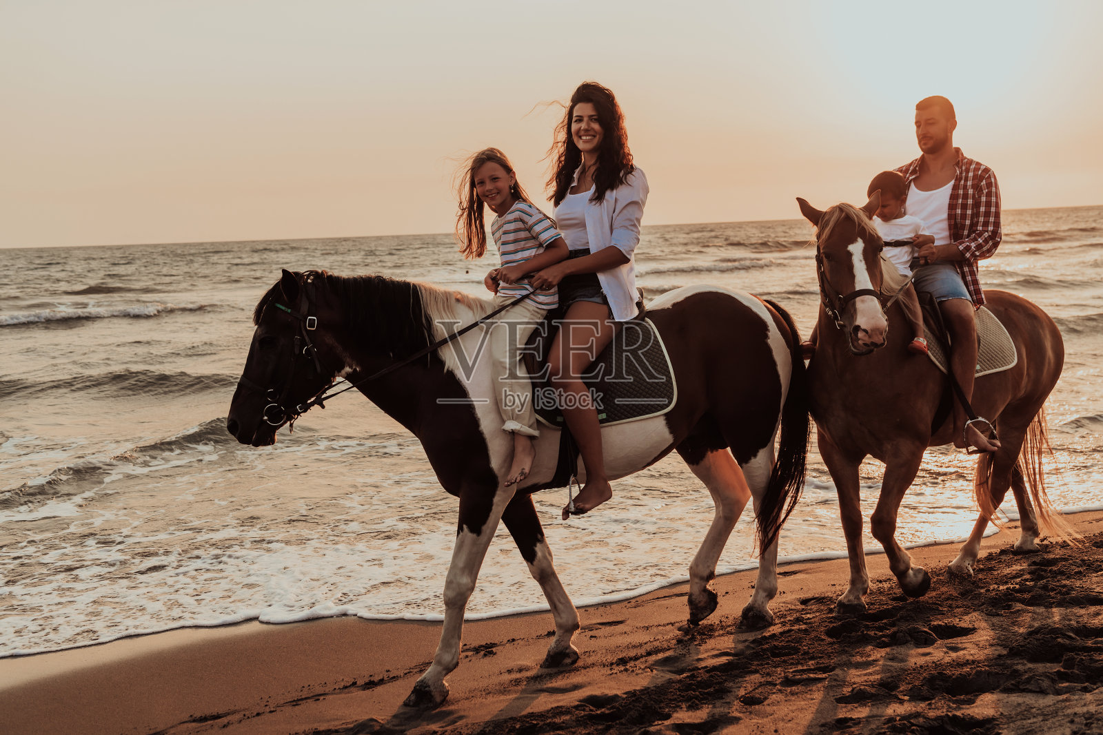 一家人和孩子们一起在沙滩上骑马。有选择性的重点照片摄影图片