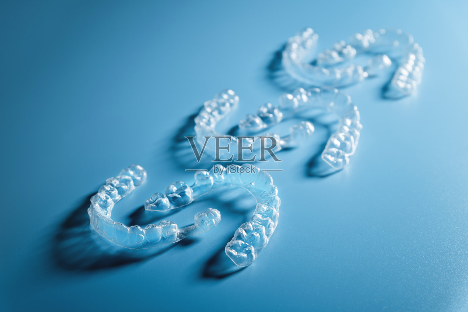 关闭蓝色背景上的不可见对齐器，并留有复制空间。矫正牙齿的塑料牙套。一组在蓝色背景上的三对对齐器照片摄影图片