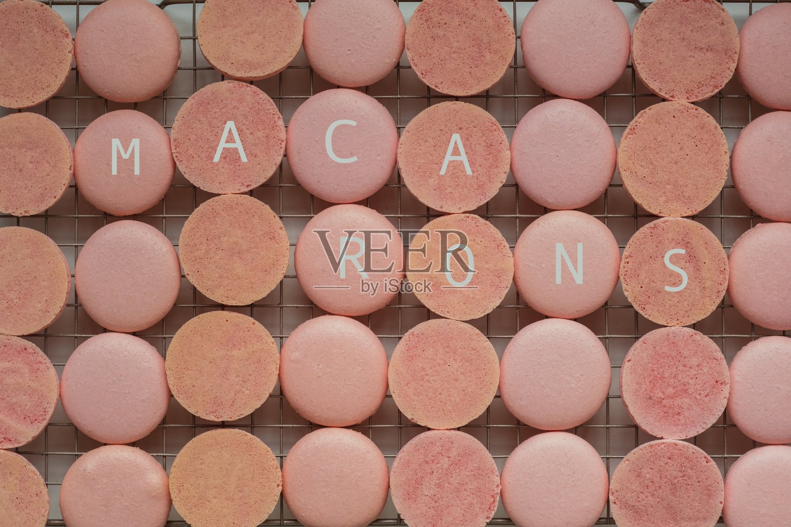 很多粉色马卡龙的一半放在冷却架上。草莓味法式甜点马卡龙的外观过程。平躺照片摄影图片