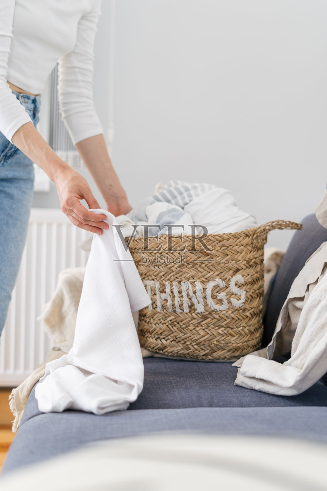 妇女把床上用品放在室内的柳条篮子里照片摄影图片