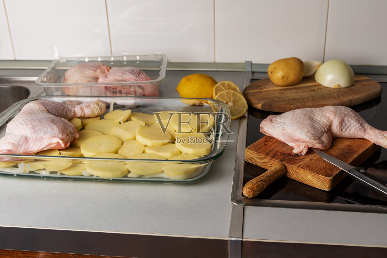 准备做柠檬鸡，烤盘里放着洋葱、土豆和鸡腿，旁边放着另一块鸡腿和柠檬，放在家庭厨房里。照片摄影图片