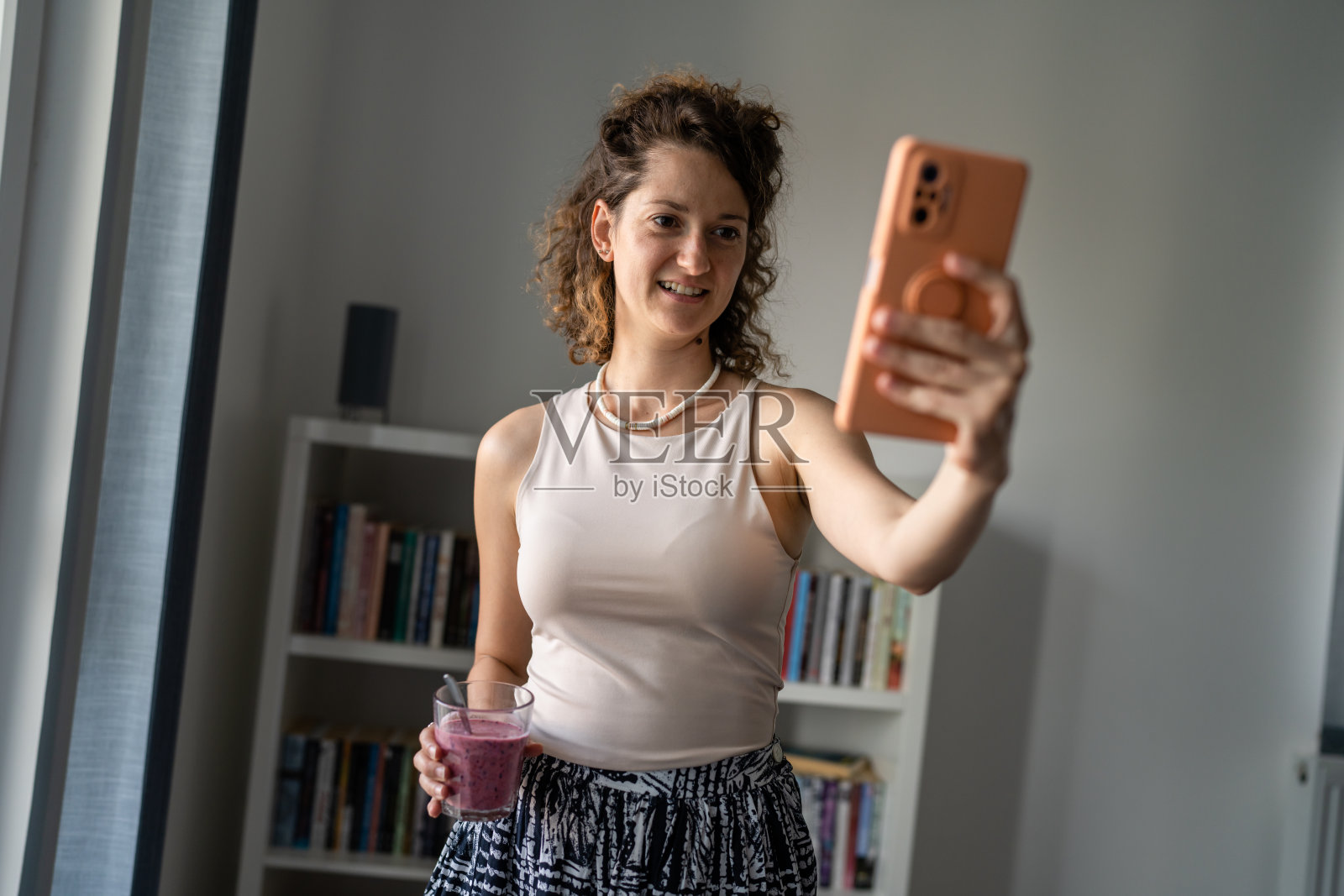 一个女人站在办公室里一边喝着冰沙一边打视频电话照片摄影图片