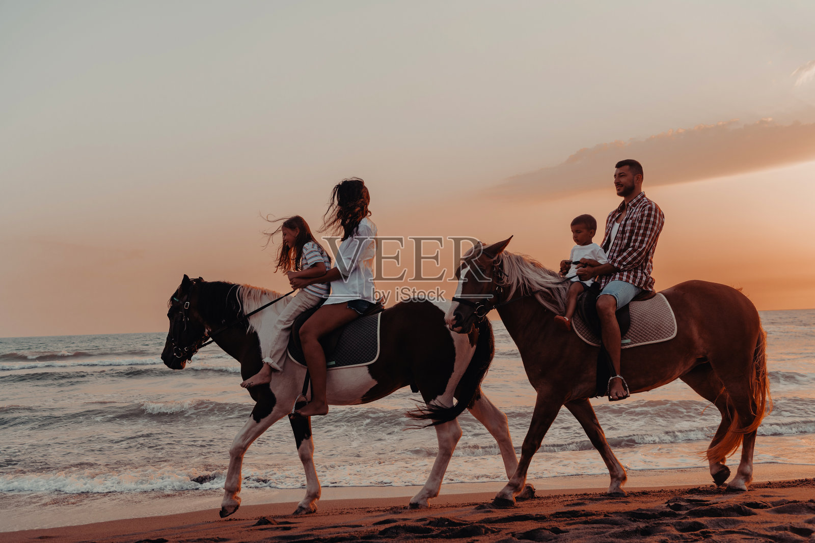 一家人和孩子们一起在沙滩上骑马。有选择性的重点照片摄影图片