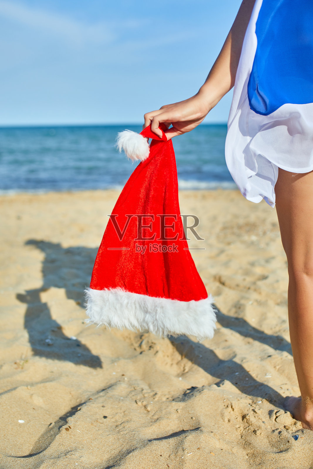 女人拿着圣诞老人的帽子站在海滩上照片摄影图片