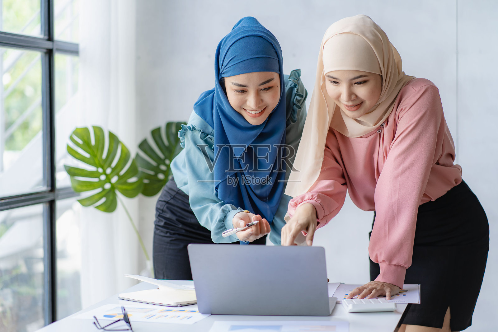 两位戴着头巾的亚洲穆斯林女性在办公室使用笔记本电脑查看财务图表照片摄影图片
