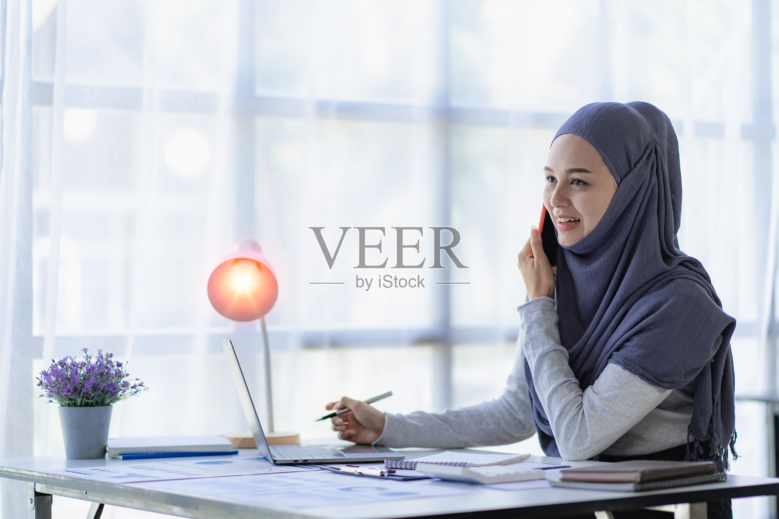 美丽的亚洲穆斯林妇女在家中使用智能手机和笔记本电脑做财务会计工作，戴着头巾照片摄影图片