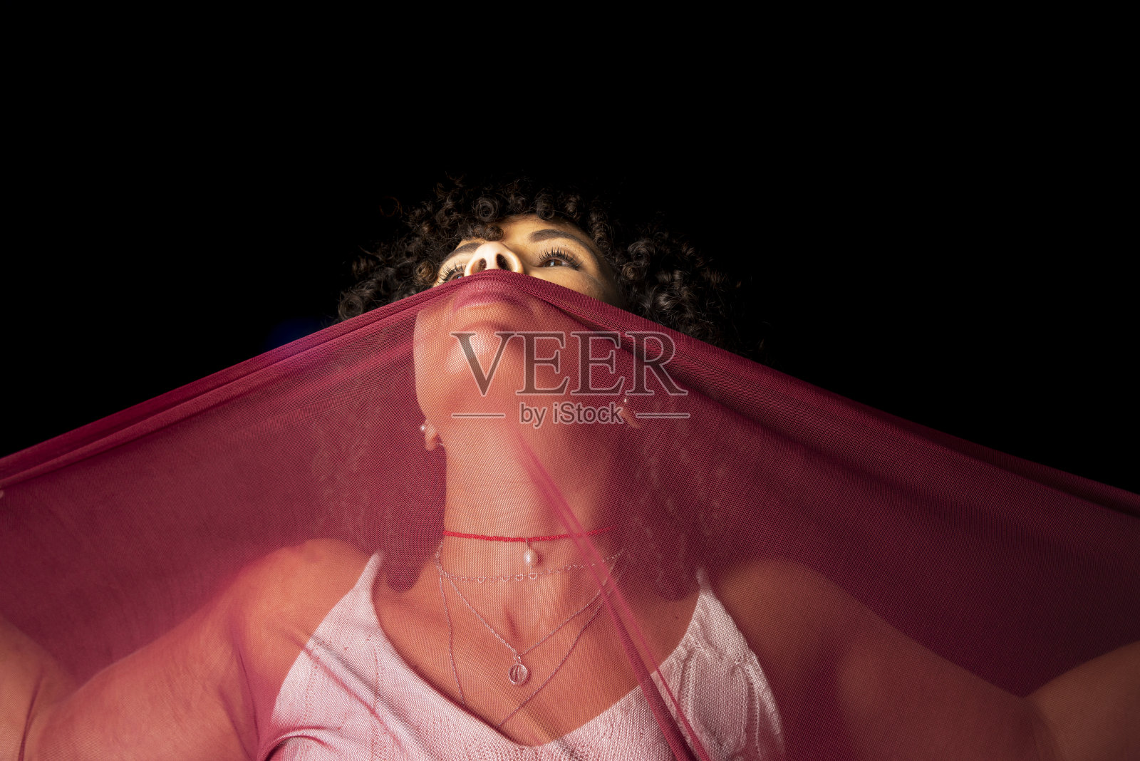 画像美丽的女人与深红色的薄布在她的脸上黑色的背景。照片摄影图片