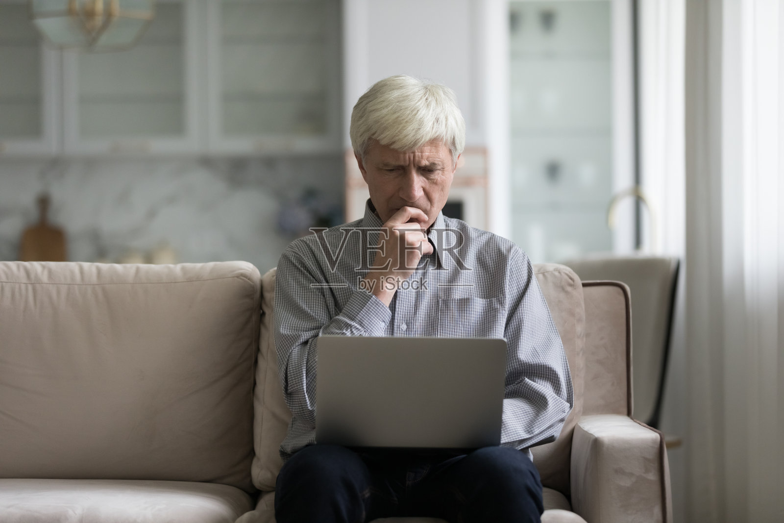 皱着眉头的老人坐在沙发上拿着笔记本电脑照片摄影图片