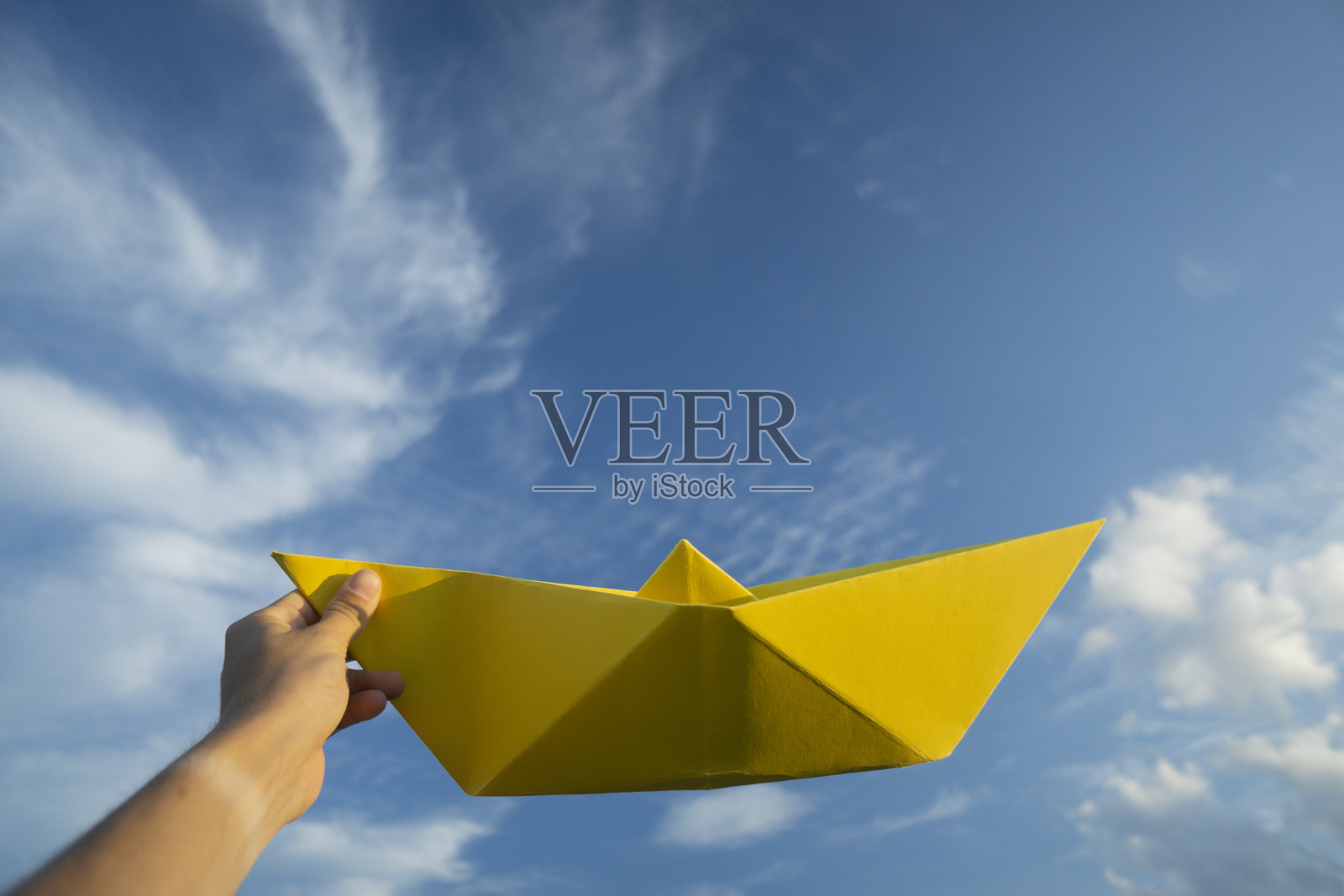一只手拿着蓝色天空背景上的黄色大纸船照片摄影图片