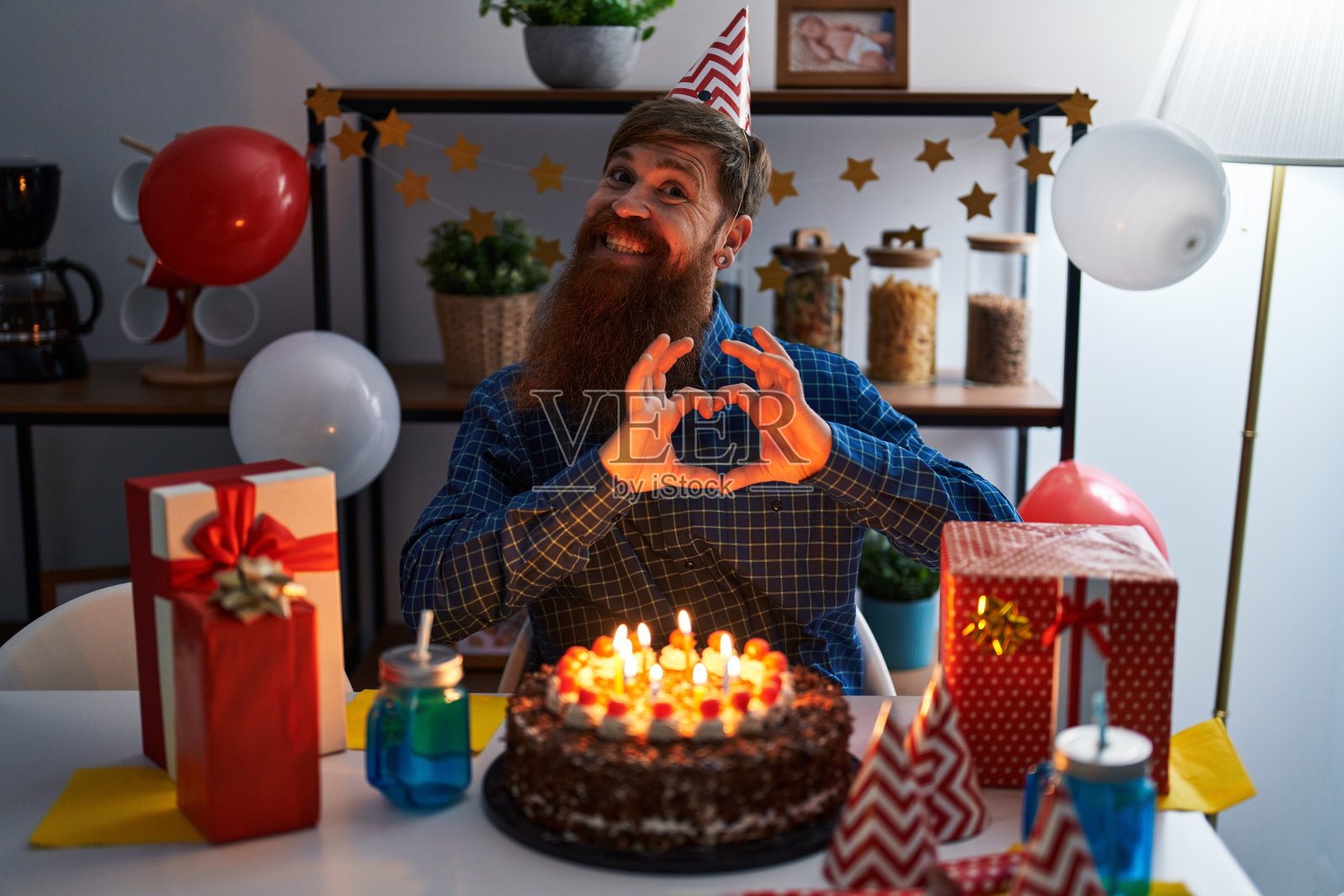 留着长胡子的白种人男子手持大巧克力蛋糕庆祝生日，用手展示心形符号和形状，面带爱意地微笑。浪漫的概念。照片摄影图片