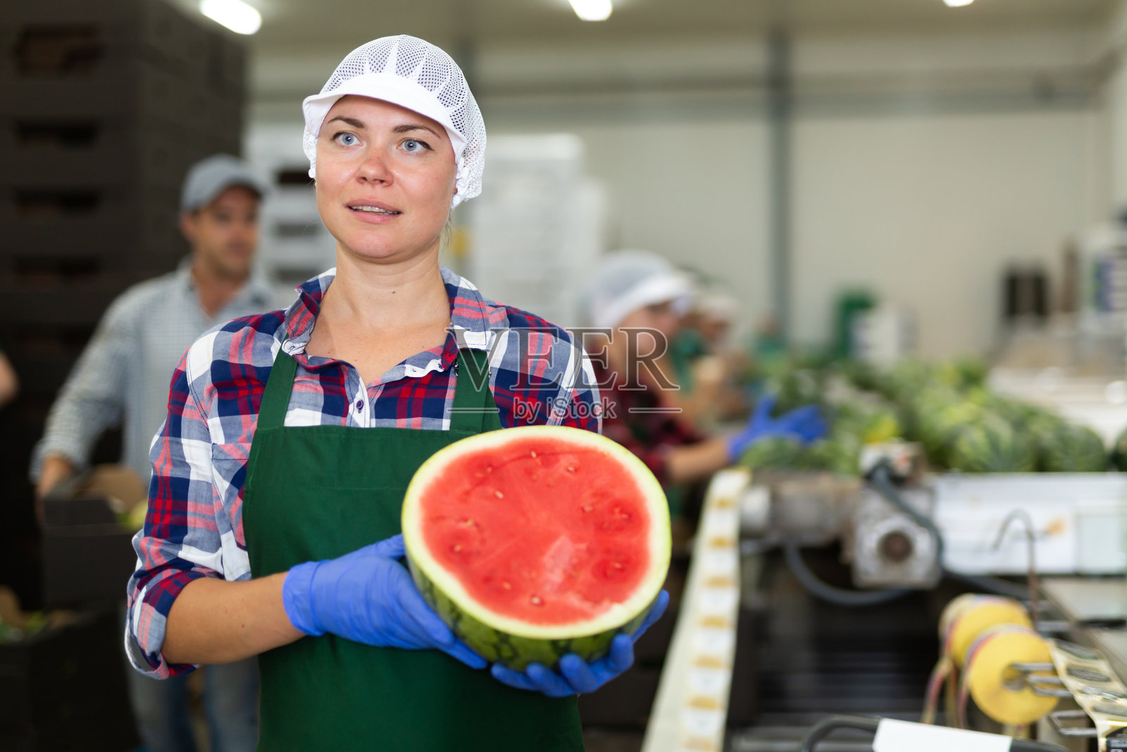 面带微笑的女工站在水果分拣厂，手里拿着半个西瓜照片摄影图片