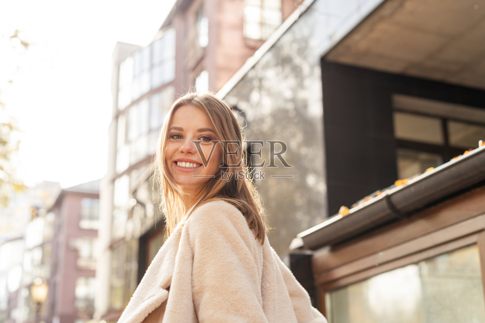 清晨，迎着温暖的阳光，妇女离开家去上班。美丽的女孩在街上回头看照片摄影图片