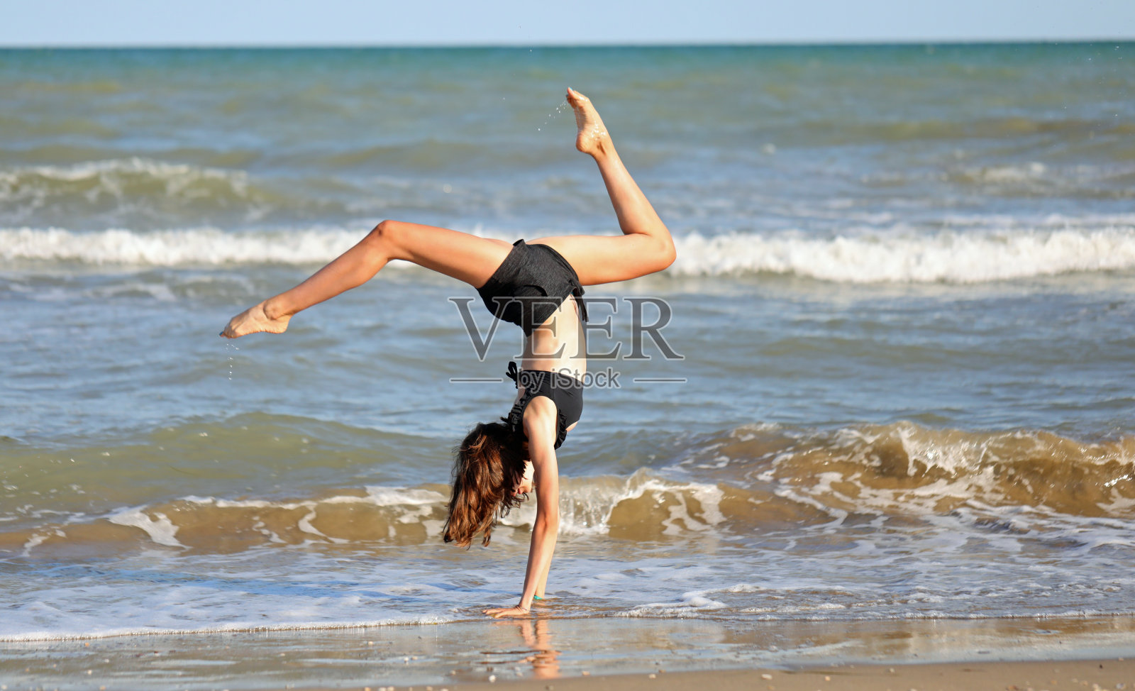 在海滨进行艺术体操练习的赤脚女孩穿着黑色泳衣照片摄影图片