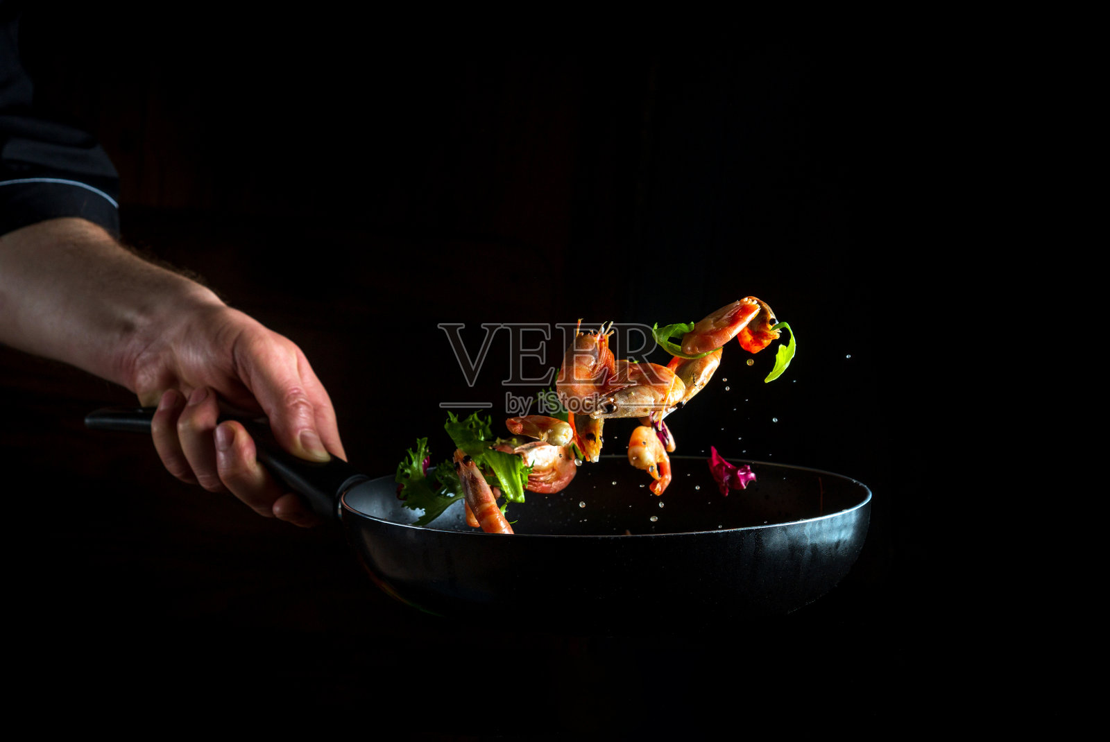 厨师在锅里和蔬菜一起煮虾。烹饪海鲜、健康素食和深色背景的食物。冻结。免费的广告空间照片摄影图片