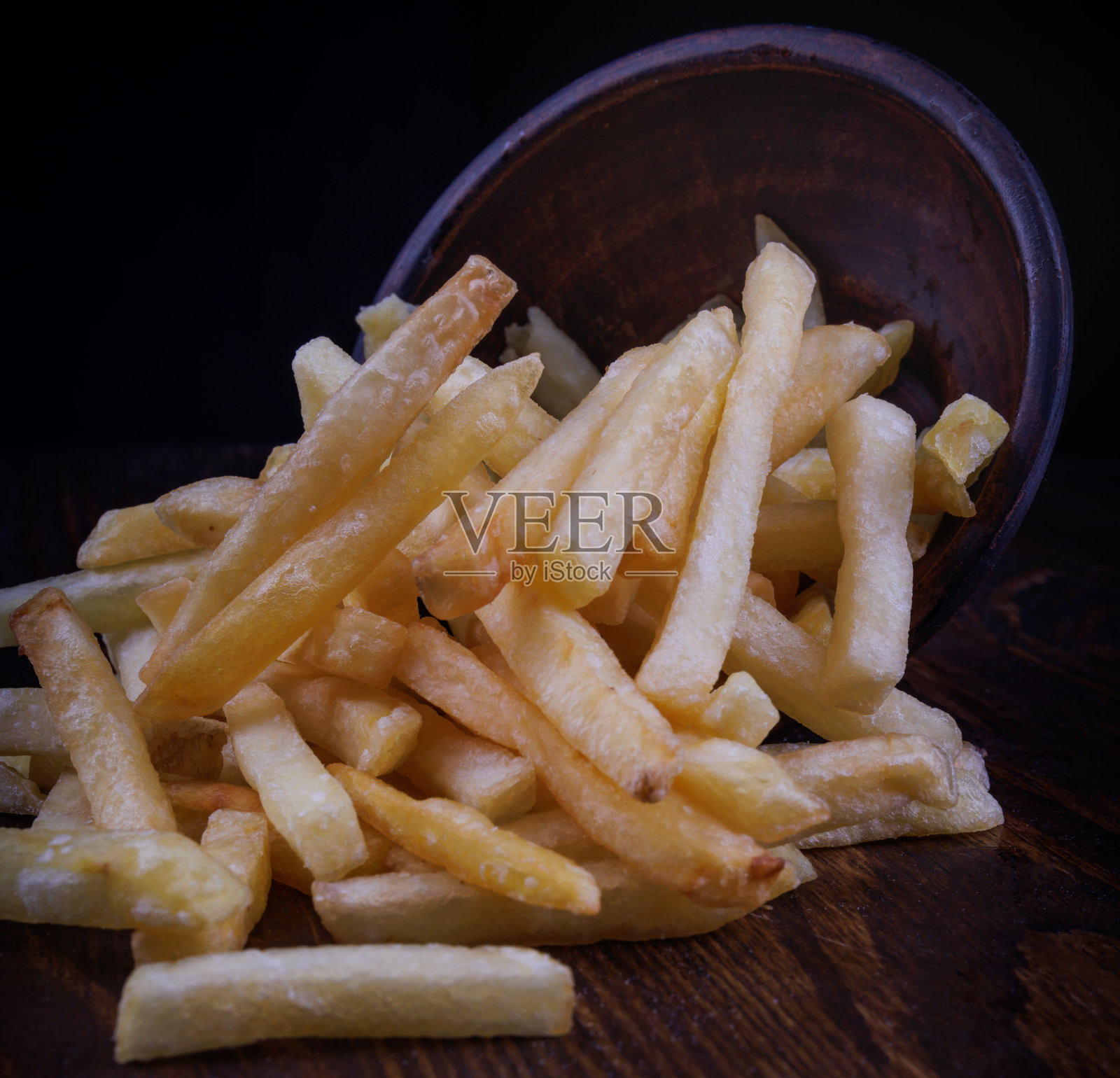 薯条装在陶罐里，散落在附近。深色背景下的炸薯条。照片摄影图片