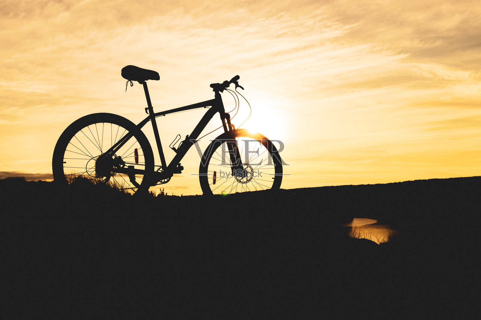 自行车剪影在山上靠近河流，橙色的日落天空和模糊的云照片摄影图片