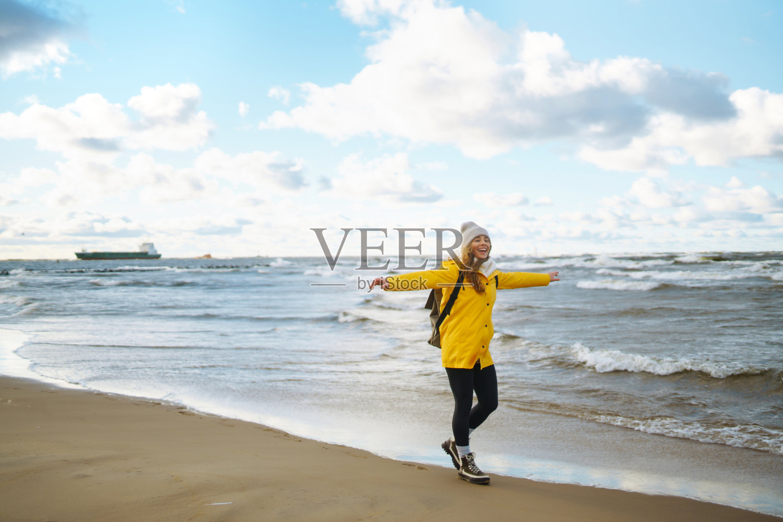 穿着黄色夹克的女游客在海边摆姿势。照片摄影图片
