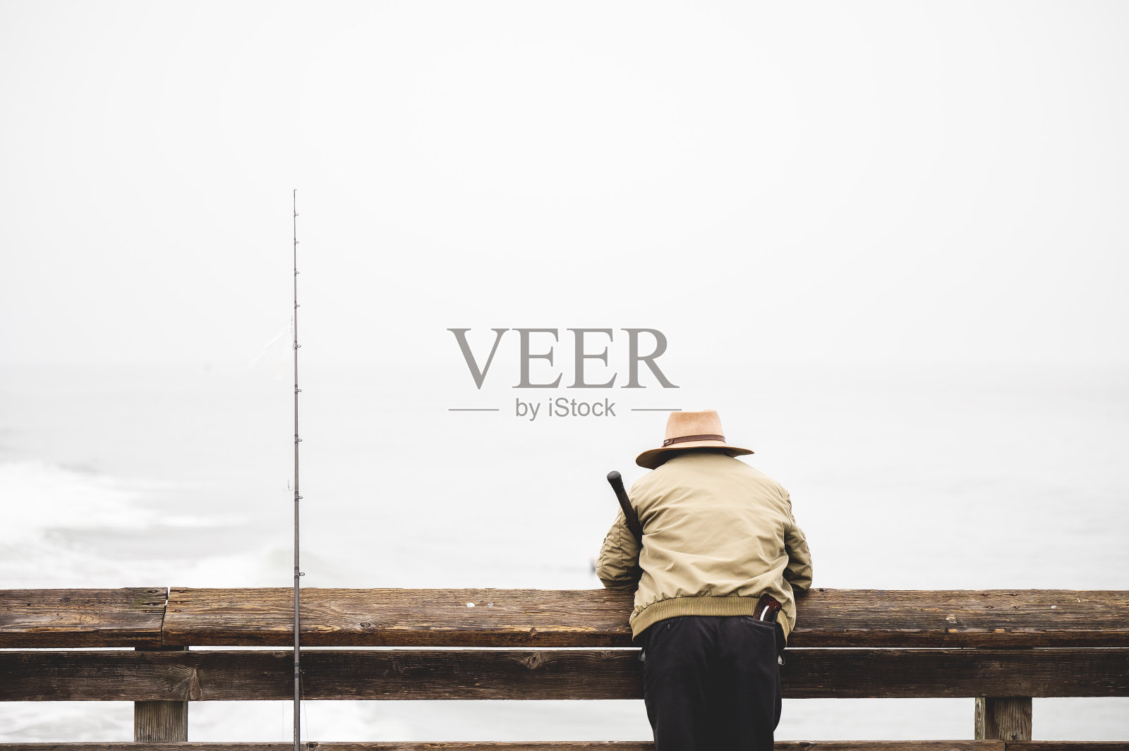 一个渔民靠在码头的木栏杆上看海岸的后景照片摄影图片