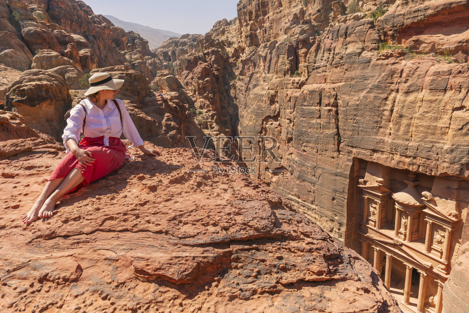 年轻的游客戴着帽子，穿着时髦的服装在Al-Khazneh(国库)，这是约旦佩特拉古城最精致的寺庙之一。从以上观点。照片摄影图片
