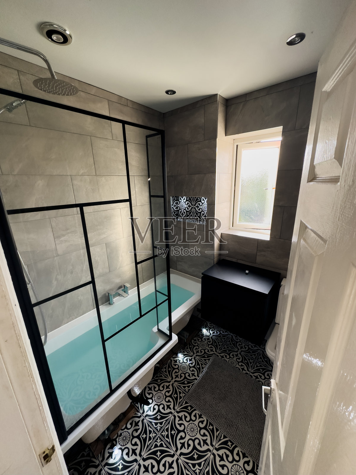 一个现代化的小浴室，有深色的水池和镜子。灰色瓷砖，镀铬淋浴和水龙头。淋浴屏幕上的黑色细节照片摄影图片