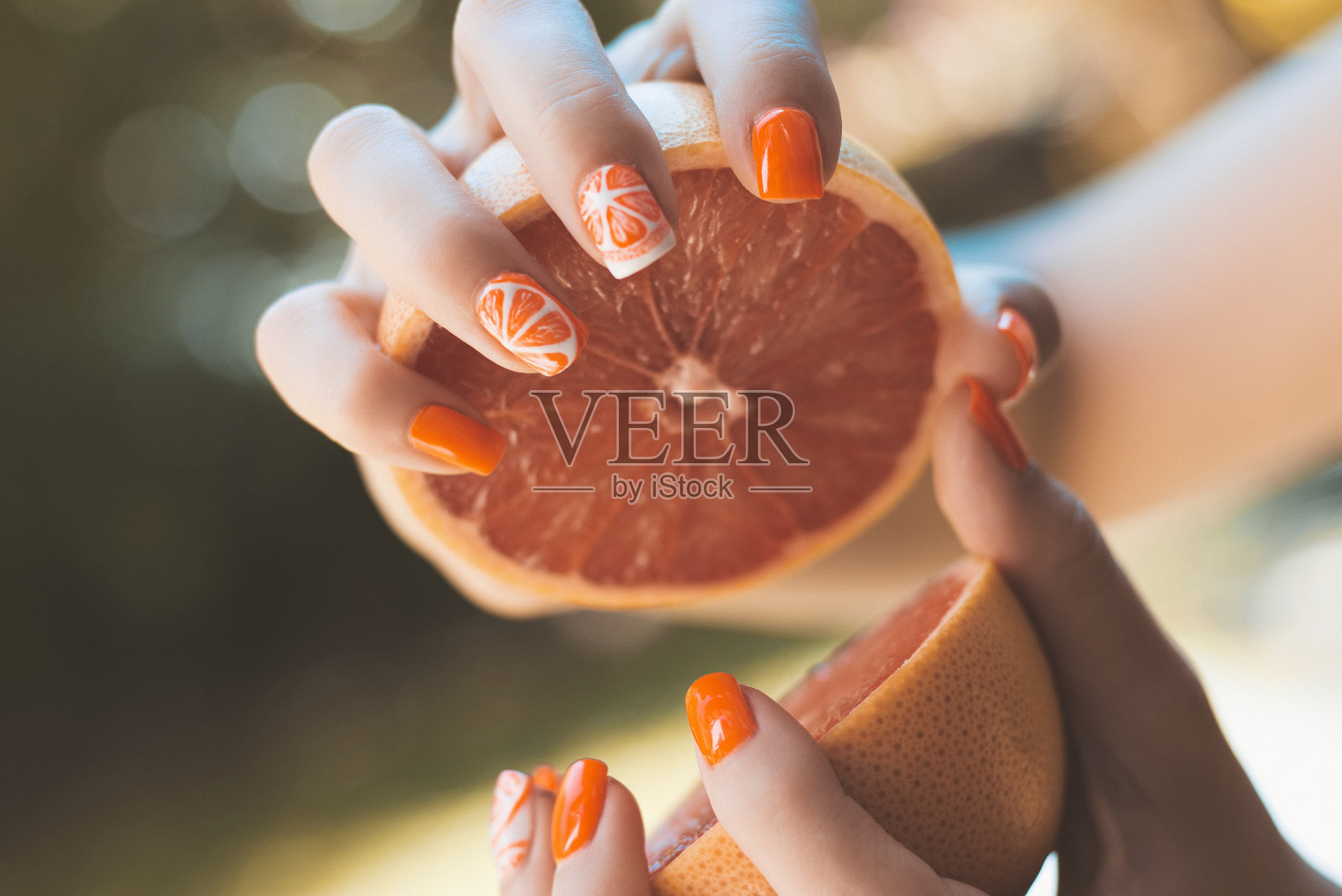 有着主题美甲的温柔女性手握切成两半的葡萄柚。艺术的指甲画概念。阳光眩光和模糊的背景，特写与选择性焦点照片摄影图片
