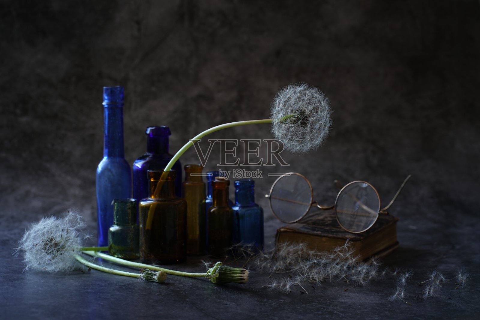 一幅静物画，由19世纪末和20世纪初的彩色小瓶子和古董玻璃杯组成，它们长着白色蓬松的头，放在深色背景的桌子上照片摄影图片