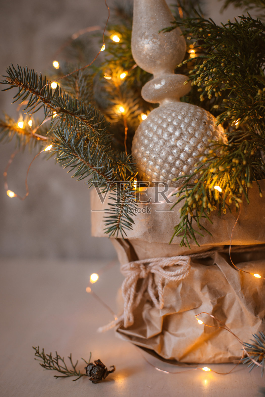 天然的圣诞花束装在工艺纸袋里，配上花环灯和玻璃顶顶装饰，衬着灰色的混凝土墙。照片摄影图片