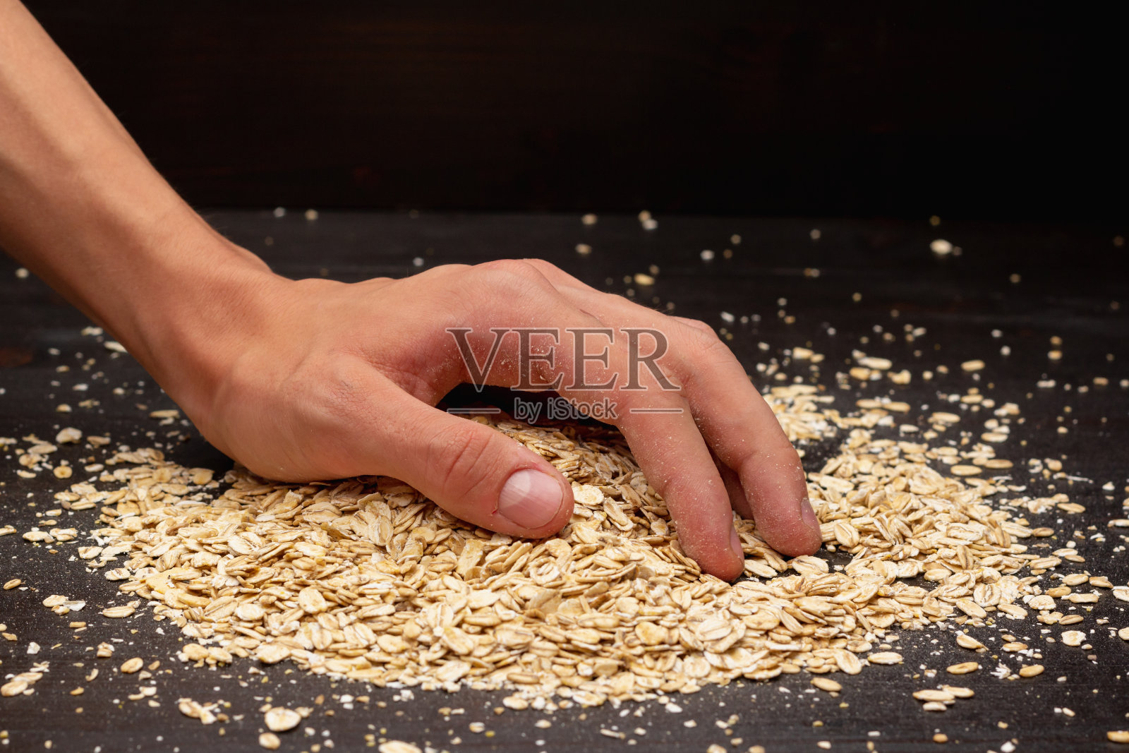 男性的手在黑色的背景上倒着什锦麦片照片摄影图片