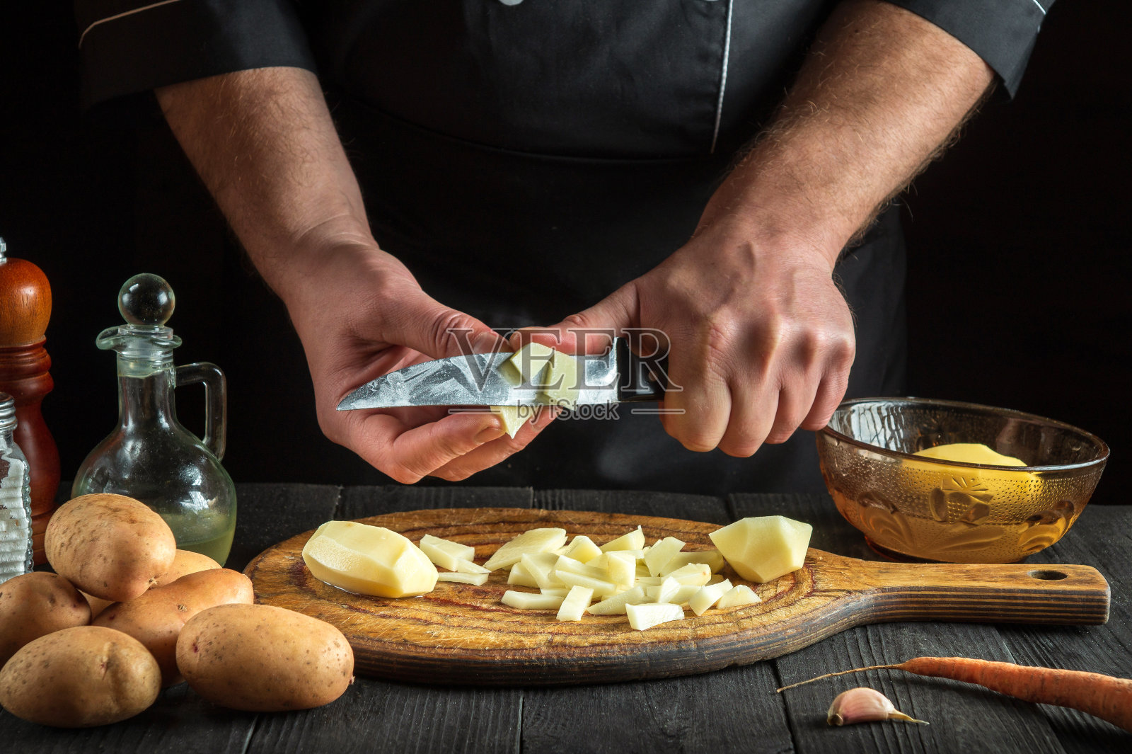 在做薯条之前，厨师用刀把生土豆切成小块。一个厨师在餐厅厨房工作的特写镜头照片摄影图片