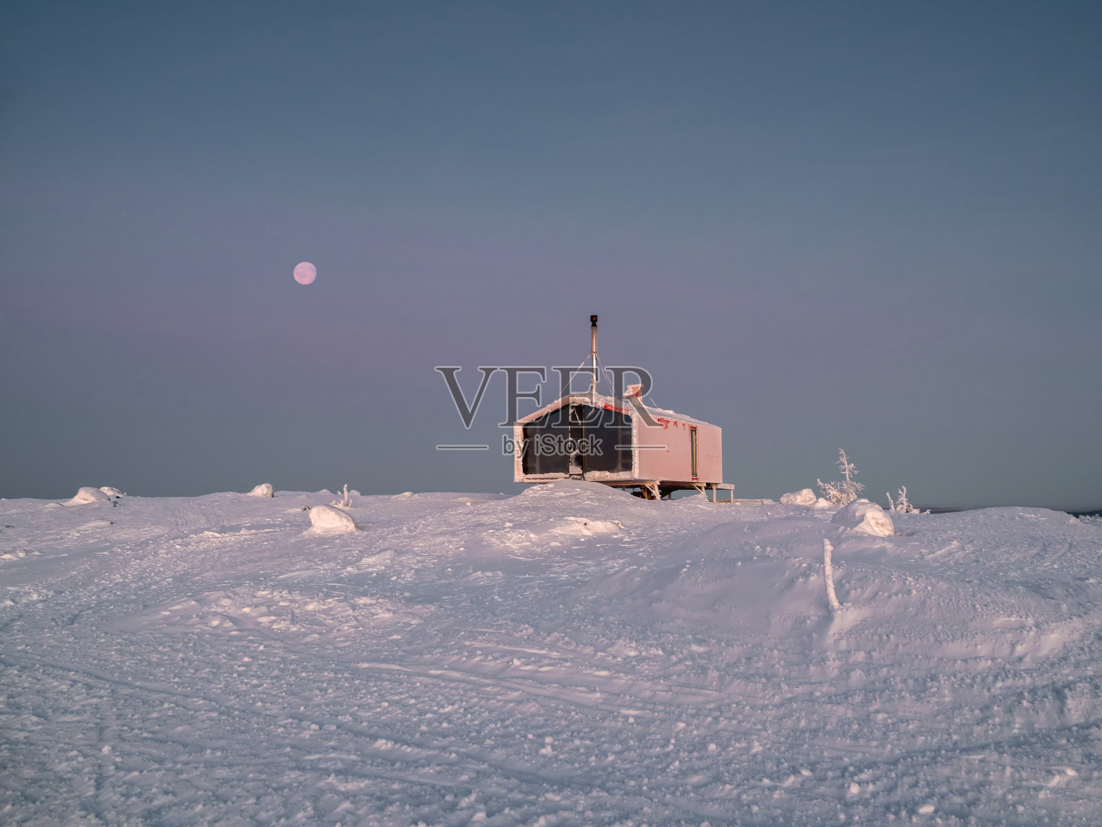 雪山山坡上的舒适小屋。黑暗的天空中有一轮红色的圆月。严酷的北方自然。照片摄影图片