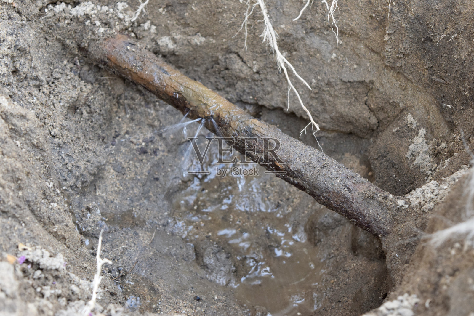 水从泥泞的管道中洒出来，管道穿过沟渠中的地面照片摄影图片