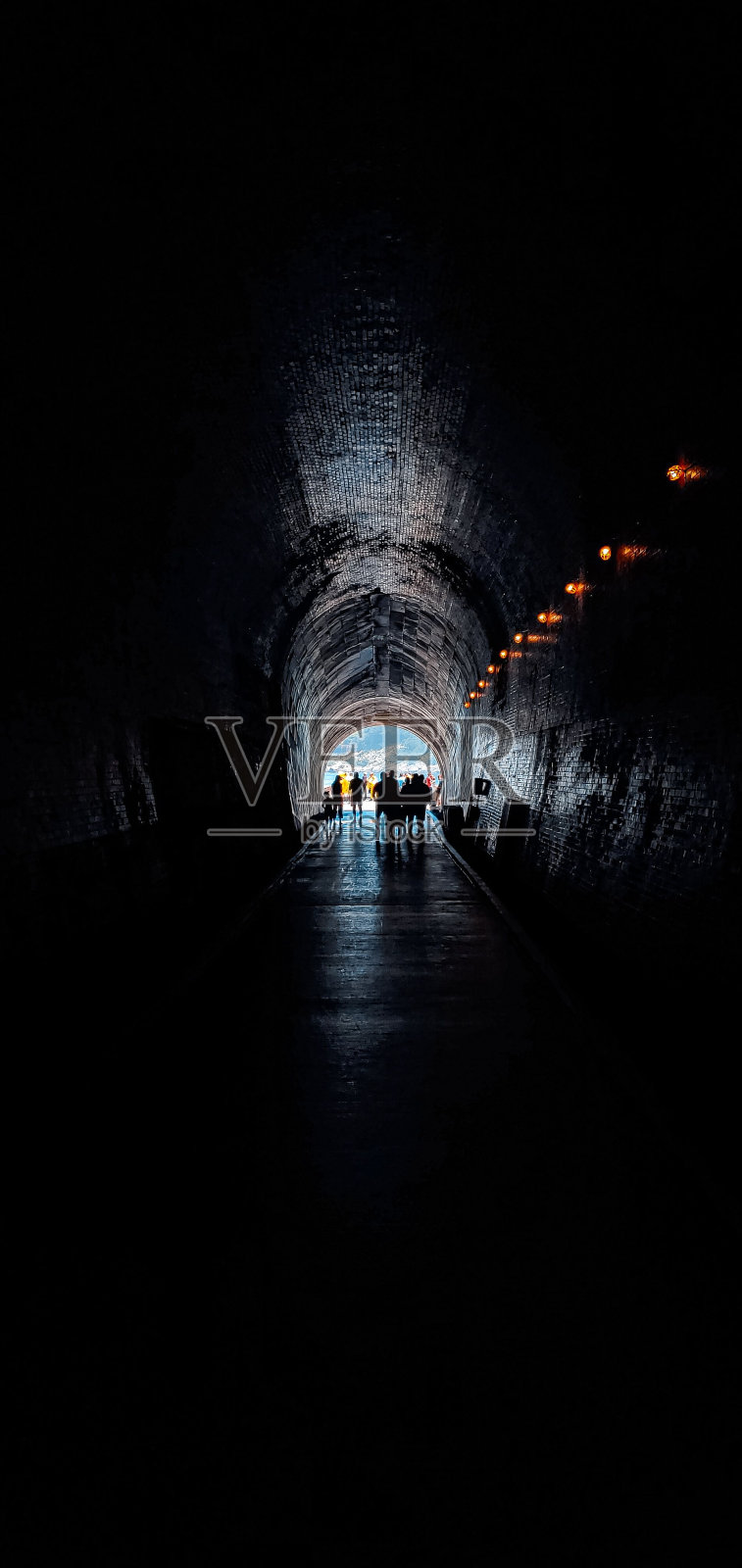 垂直拍摄的人们走在黑暗狭窄的隧道，通向美丽的风景照片摄影图片