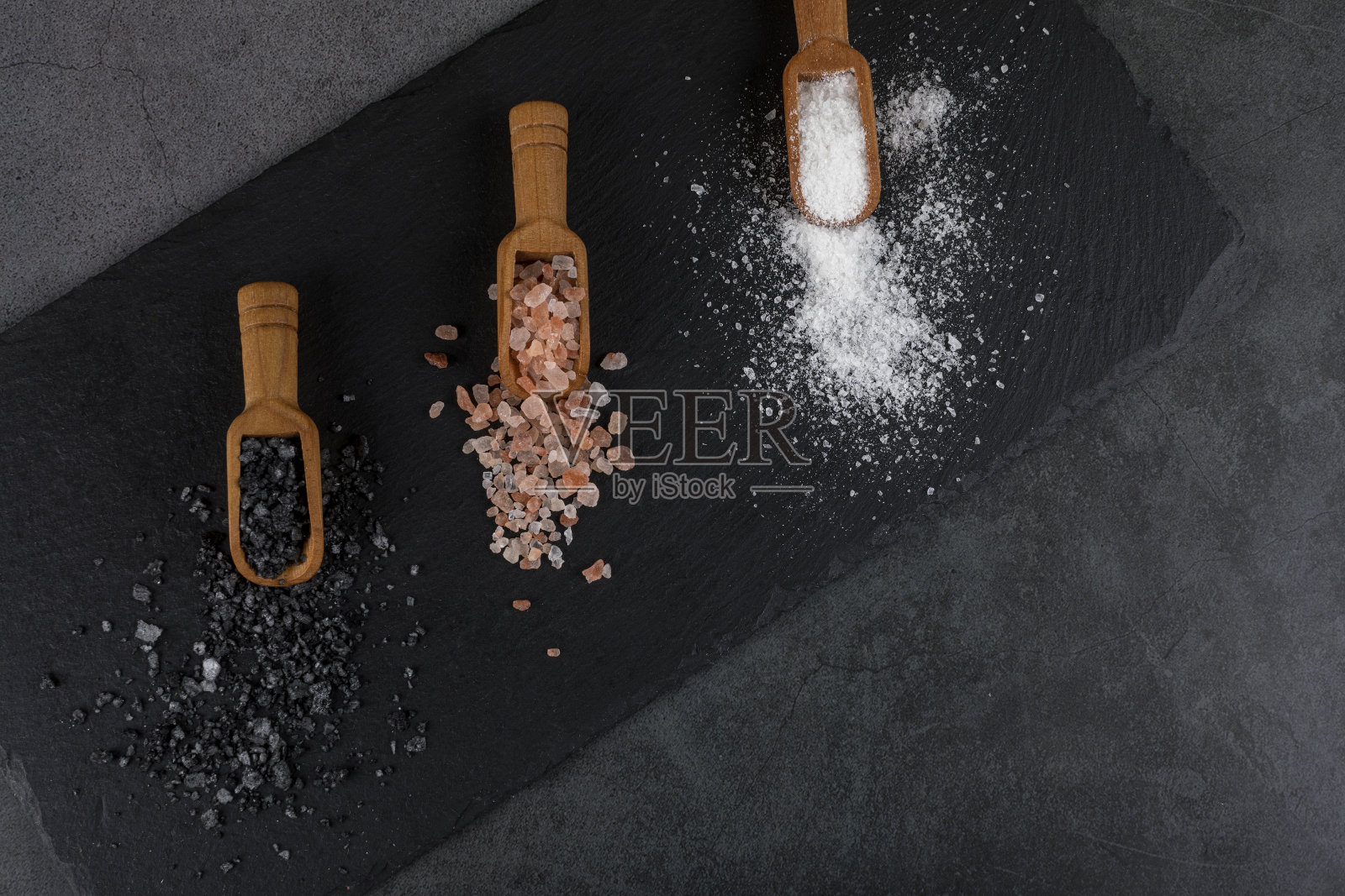 不同种类的盐。白色的海盐，粉红色的喜马拉雅盐和黑色的火山盐放在三个木勺里。照片摄影图片