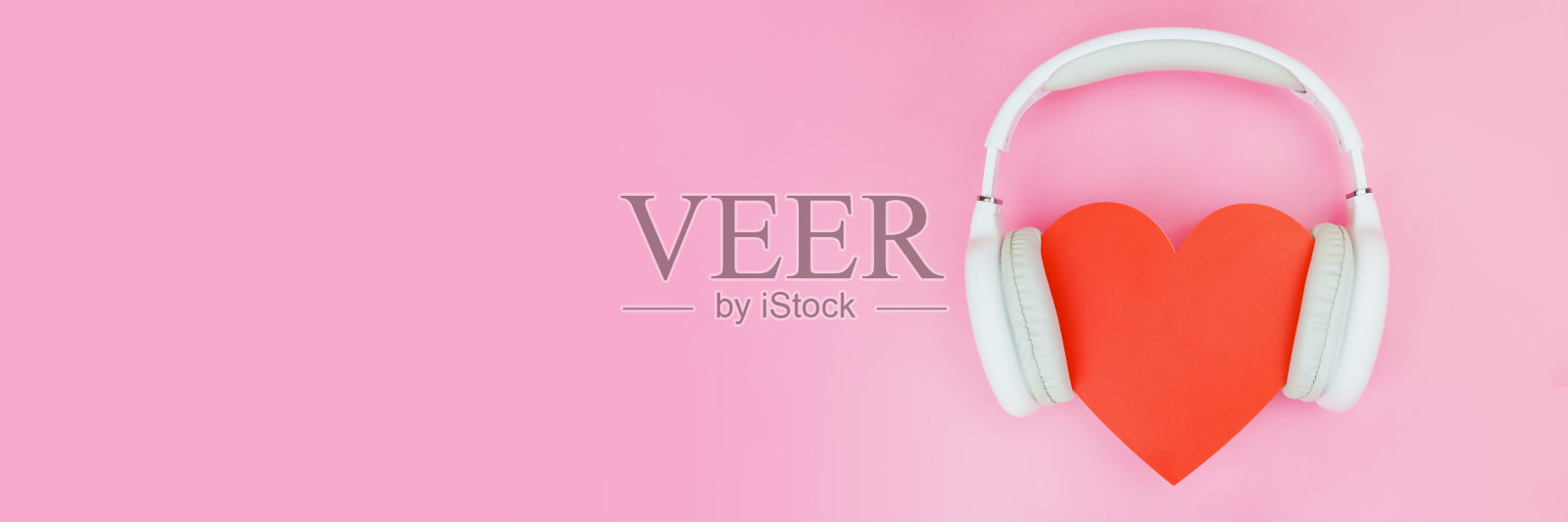 白色的无线耳机戴在粉色背景上的红心上照片摄影图片