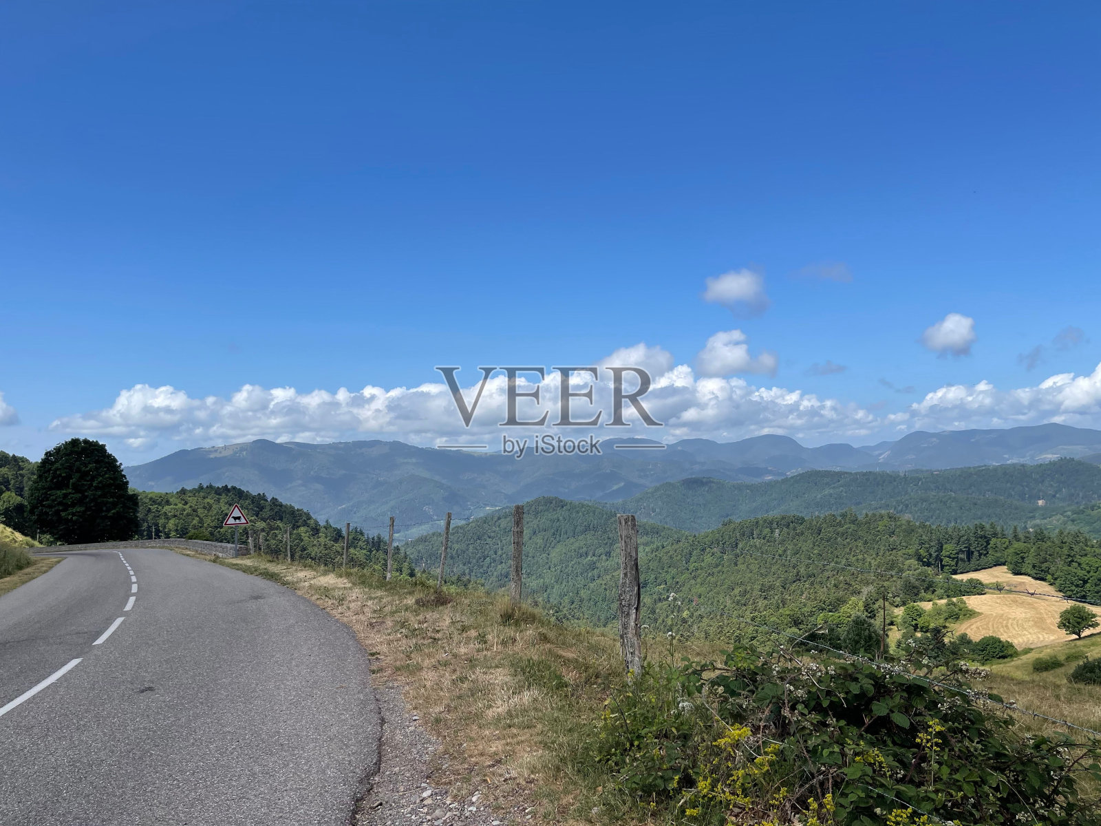 沿着山边的柏油路，可以看到蓝天白云下的青山照片摄影图片