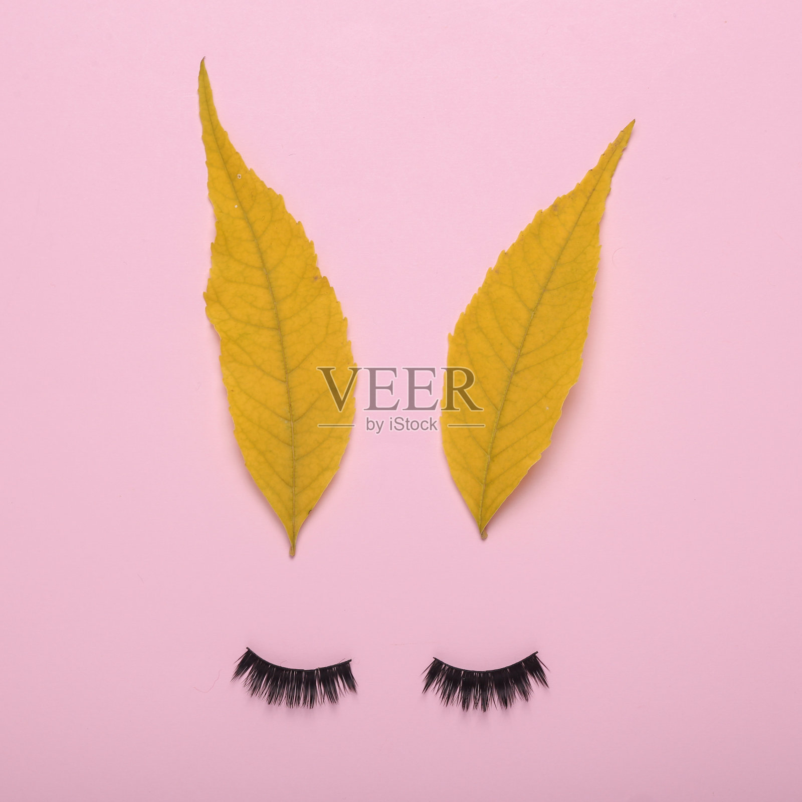 复活节的概念。可爱的兔子脸由假睫毛和黄色的树叶在粉红色的背景照片摄影图片