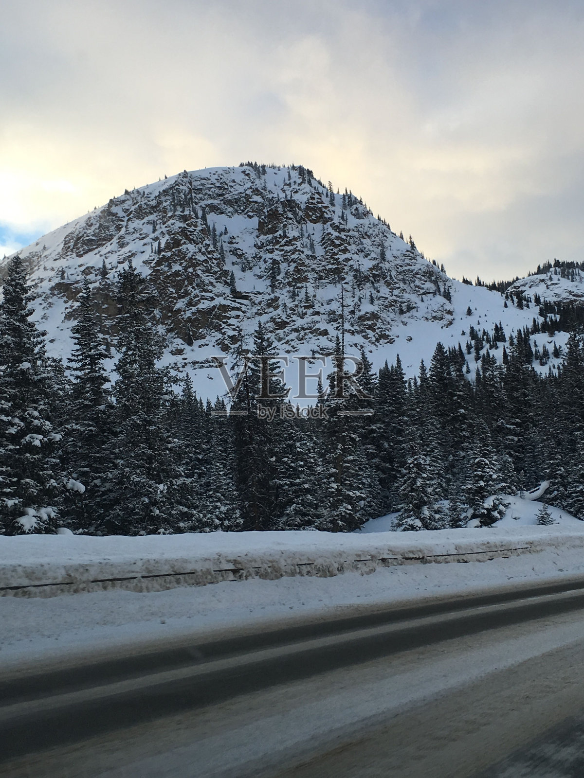 垂直拍摄的积雪覆盖的树在山上和结冰的道路在多云的天空照片摄影图片