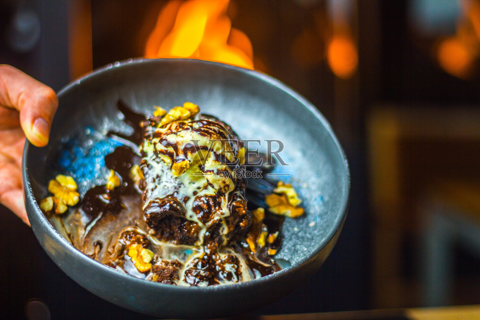 男子拿着一碗美味的巧克力蛋糕，上面有冰淇淋球和核桃照片摄影图片