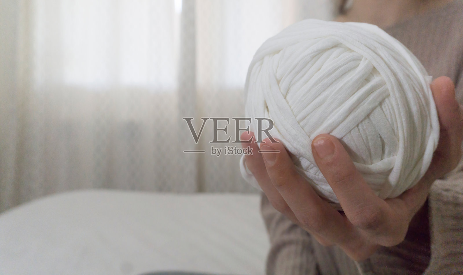 在模糊的背景上，一只手拿着一个白色t恤纱线球的特写照片摄影图片