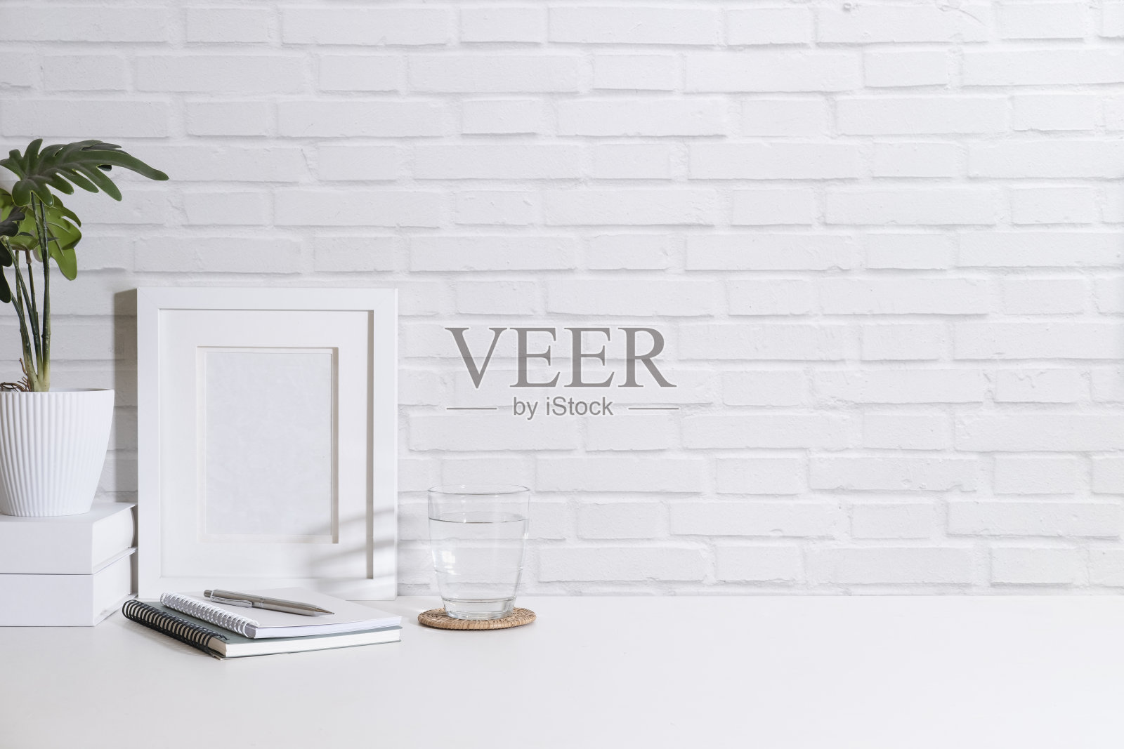 白色的相框，盆栽，一杯水，笔记本放在靠砖墙的白色桌子上。复制空间为您的广告文本。照片摄影图片