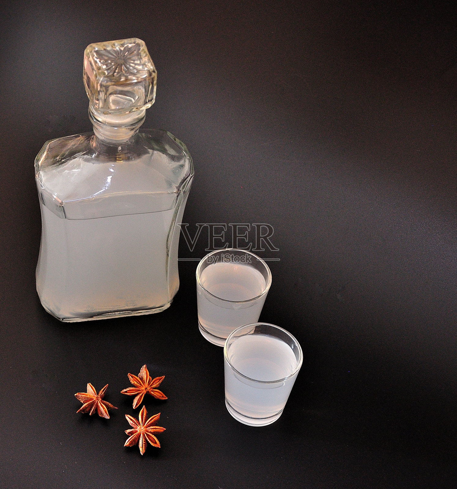 一瓶八角利口酒，黑色背景上有两个把手，旁边是干果。照片摄影图片